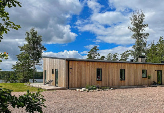 Moderna villa in legno sul lago in Svezia circondata da alberi, cielo blu e natura incontaminata.