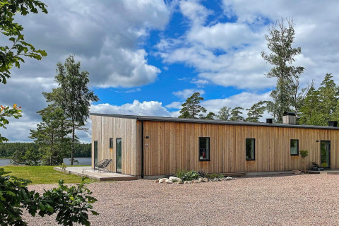 Moderna villa in legno sul lago in Svezia circondata da alberi, cielo blu e natura incontaminata.