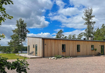 Moderne houten villa aan het meer in Zweden, omgeven door bomen, blauwe lucht en natuurschoon.