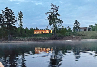 Foto serale della Spacious Lakeside Villa con finestre illuminate sul lago, circondata da alberi in Svezia.