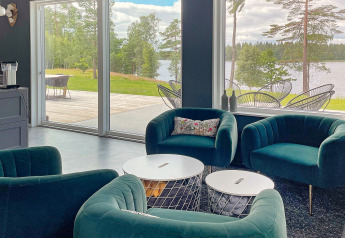 Salotto moderno in una villa sul lago in Svezia con poltrone verdi, grandi finestre e vista panoramica.
