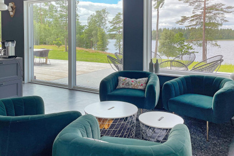 Modern lounge in a Swedish lakeside villa with green armchairs, large windows, and scenic lake views.