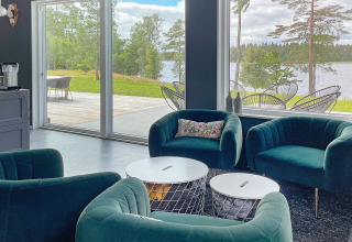 Salotto moderno in una villa sul lago in Svezia con poltrone verdi, grandi finestre e vista panoramica.