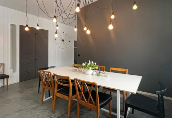 Eetkamer in een ruime villa aan het meer in Zweden, met moderne verlichting en houten stoelen.