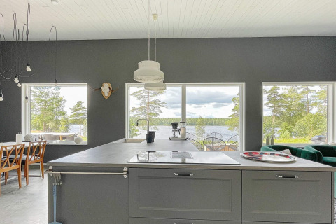 Moderne Küche mit großen Fenstern, Seeblick und bewaldeter Landschaft in einer schwedischen Villa.