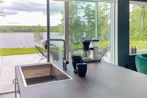 Moderne Kücheninsel mit Spüle und Kaffeemaschine, Panoramablick auf See im schwedischen Ferienhaus.