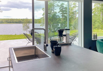 Moderne keukeneiland met gootsteen en koffiezetapparaat, uitzicht op meer in Zweedse villa.