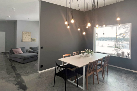 Sala da pranzo moderna in una villa svedese sul lago, lampadine sospese e vista su un lago ghiacciato.