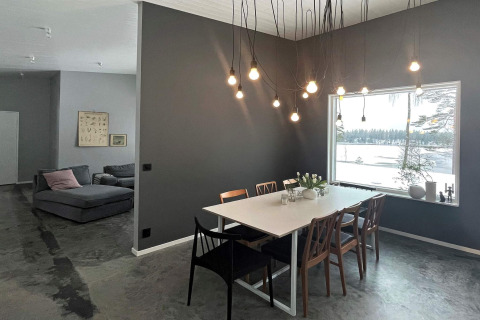 Sala da pranzo moderna in una villa svedese sul lago, lampadine sospese e vista su un lago ghiacciato.