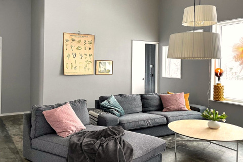 Soggiorno moderno e luminoso di una spaziosa villa sul lago in Svezia con divano grigio e finestre ampie.