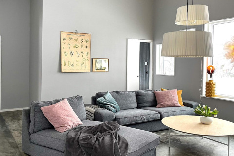 Soggiorno moderno e luminoso di una spaziosa villa sul lago in Svezia con divano grigio e finestre ampie.