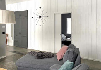 Moderne woonkamer in lodge met grijs interieur, wandklok en schuifdeur naar slaapkamer in Zweden.
