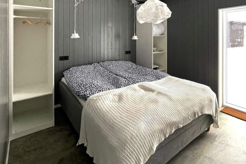 Chambre dans une villa suédoise au bord du lac, murs gris, lit double, couette blanche et placard ouvert.