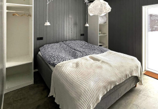 Bedroom in Swedish lakeside villa with gray paneled walls, double bed, white blanket, and open closet.