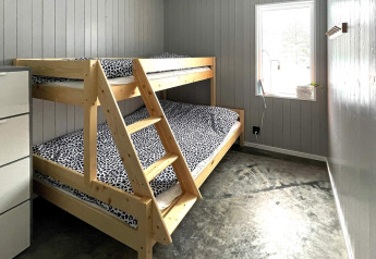 Habitación en una cabaña con litera, ropa de cama de leopardo, paredes grises y ventana, Suecia.
