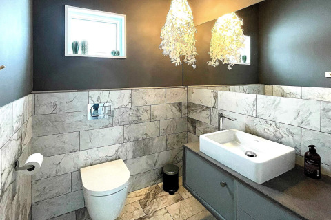 Baño moderno con azulejos de mármol, inodoro suspendido y luces decorativas, en villa sueca.