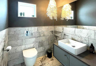 Modernes Badezimmer mit Marmorboden und -wänden, wandhängendem WC und Designerlampe in einer Villa.