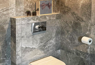 Bagno moderno con piastrelle in marmo grigio, WC sospeso, cassetta nascosta e piante decorative sulla mensola.