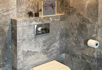 Bagno moderno con piastrelle in marmo grigio, WC sospeso, cassetta nascosta e piante decorative sulla mensola.