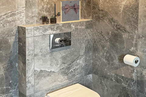 Bagno moderno con piastrelle in marmo grigio, WC sospeso, cassetta nascosta e piante decorative sulla mensola.