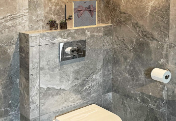 Moderne badkamer met grijze marmeren tegels, hangtoilet, verborgen reservoir en decoratieve planten op de plank.