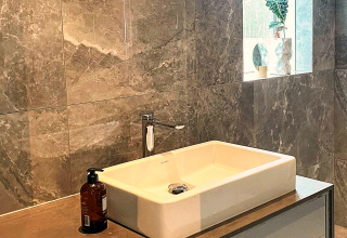 Bagno moderno in marmo con lavabo quadrato, dispenser di sapone e pianta su finestra in villa svedese sul lago.