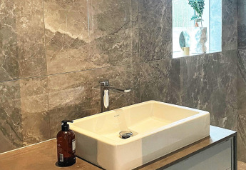 Moderne badkamer met vierkante wasbak, zeeppompje en raam met plant in een Zweedse lodge aan het meer.
