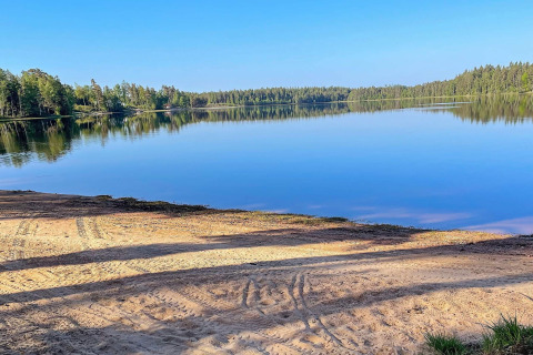 Ruhiger Blick auf einen See mit sandigem Ufer und Wald bei Spacious Lakeside Villa with in Schweden.