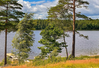 Panorama di lago con alberi verdi, cielo azzurro e piccolo molo vicino a una villa in Svezia.