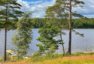 Scenic lakeside view in Sweden showing calm water, lush trees, blue sky, and a small dock in the foreground.