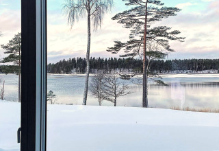 Vista dalla finestra del lodge su un lago innevato e pini presso Spacious Lakeside Villa with in Svezia.