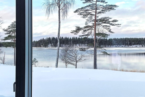 Vue depuis la fenêtre du lodge sur un lac enneigé et des pins à Spacious Lakeside Villa with en Suède.