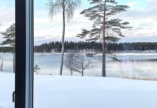 Vista desde la ventana del albergue a un lago cubierto de nieve y pinos en Spacious Lakeside Villa with en Suecia.