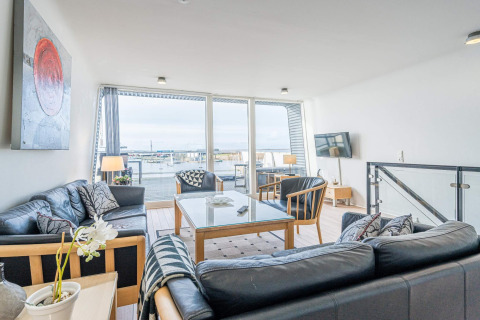 Soggiorno su houseboat con divani moderni e grandi finestre vista porto a Hemmet, Danimarca.