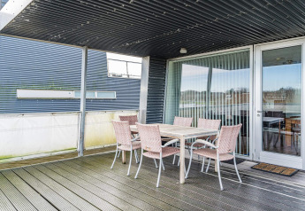 Überdachte Terrasse eines Hausbootes mit Esstisch und sechs Stühlen im 6-Personen-Ferienhaus in Hemmet, Dänemark.