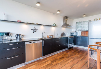 Cocina moderna en casa flotante con gabinetes negros, suelo de madera y electrodomésticos de acero en Hemmet, Dinamarca.
