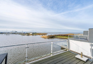 Uitzicht vanaf het terras van een woonboot in Hemmet, Denemarken, op water, riet en een jachthaven.