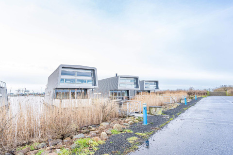 Moderne woonboten aan het water in Hemmet, Denemarken, omringd door riet en een verharde parkeerplaats