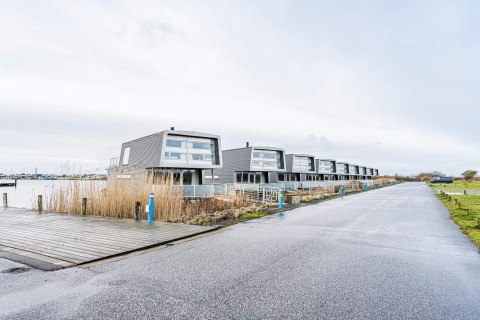 Moderne husbåde ved kajen i Hemmet, Danmark, omgivet af vand, vej og grønne områder.