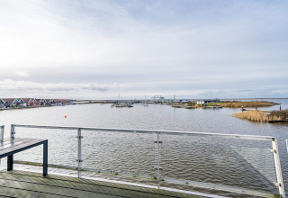 Udsigt fra en husbåd på Hemmet i Danmark med vand, både, rækværk og ferieboliger i baggrunden.