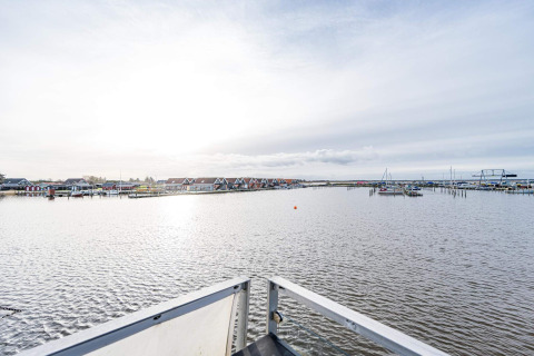 Uitzicht vanaf een woonboot in Hemmet, Denemarken, met water, boten en kleurrijke huisjes aan wal.