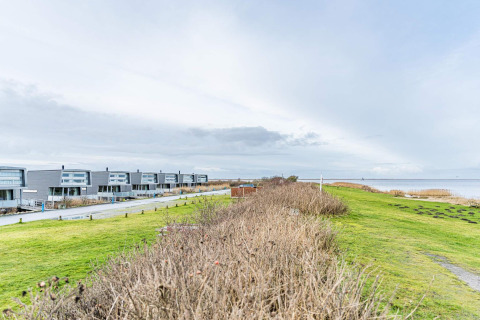 Moderne Hausboote am Ufer in Hemmet, Dänemark, mit Blick auf grüne Flächen und das Meer.