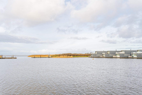 Udsigt over vandet med moderne husbåde og siv i Hemmet, Danmark under en overskyet himmel.