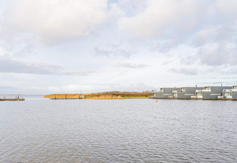 Vue sur l’eau avec des péniches modernes et des roseaux à Hemmet, Danemark, sous un ciel nuageux.