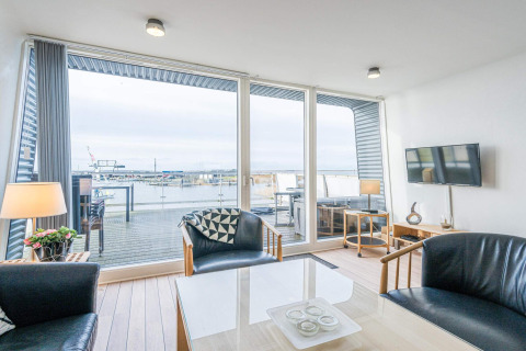 Woonkamer op een woonboot in Hemmet, Denemarken, met moderne meubels, grote ramen en uitzicht op de haven.