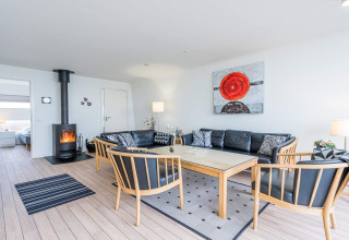 Stue med moderne sort lædersofa, brændeovn og kunstværk i et feriehus i Hemmet, Danmark.