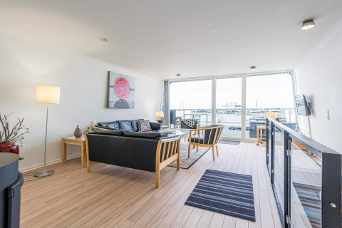 Helles Wohnzimmer auf einem Hausboot in Hemmet, Dänemark, mit moderner Einrichtung und Blick auf den Hafen.