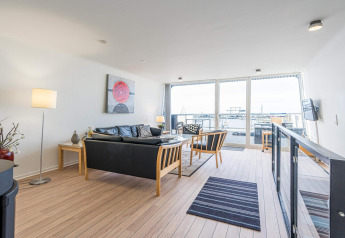 Bright living room on a houseboat in Hemmet, Denmark, with modern decor and marina views through large windows.