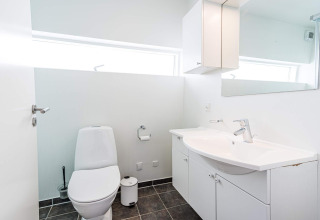 Baño moderno y luminoso con inodoro, lavabo, espejo y almacenaje en una casa flotante en Hemmet, Dinamarca.