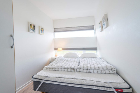 Camera da letto luminosa e compatta con letto matrimoniale, arredo moderno e finestra su houseboat a Hemmet, Danimarca.